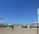 Foto de João Mattos mostra a praia de Atlântida com céu azul, pessoas na orla e placa de balneabilidade