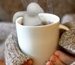 Imagem de mãos segurando uma xícara de chá com um porta-chá que é um bonequinho agarrado à beirada da xícara