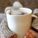 Imagem de mãos segurando uma xícara de chá com um porta-chá que é um bonequinho agarrado à beirada da xícara