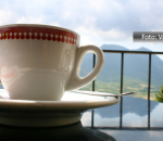 Xícara de café sobre uma mesa, com um fundo de morros e céu nublado