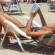 Mulher de biquíni lê um livro à beira-mar, deitada de costas em sua cadeira de praia