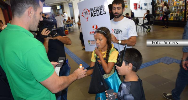 Crianças vestidas de super-heróis distribuem panfletos no aeroporto sobre o aedes. A ação é do Simers