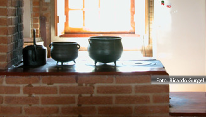 Cheleira e duas panelas de ferro sobre fogão montado em bancada de pedra